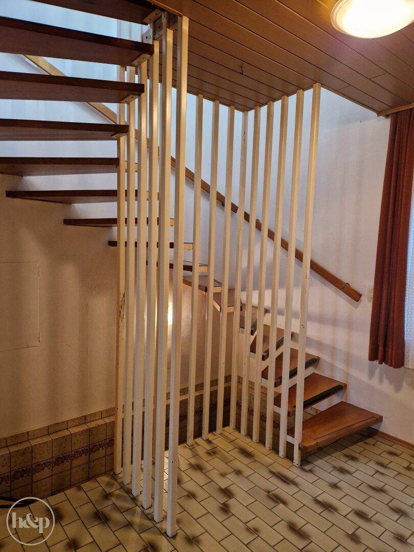 Holztreppe mit weißem Geländer und Holzdecke, die in die obere Etage führt.
