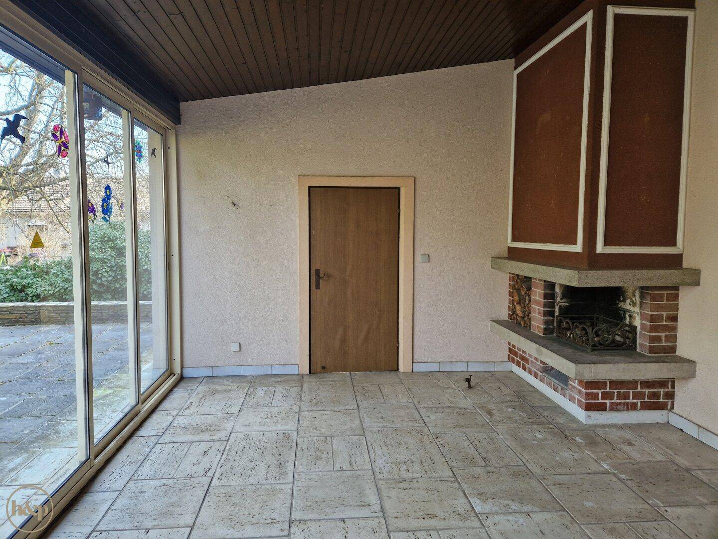 Heller Wintergarten mit Fliesenboden, Kamin und Zugang zur Terrasse.