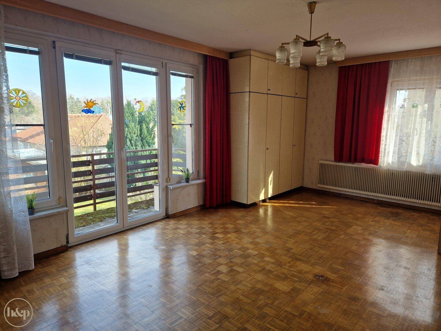 Helles Zimmer mit Parkettboden, großem Fenster und Zugang zum Balkon.