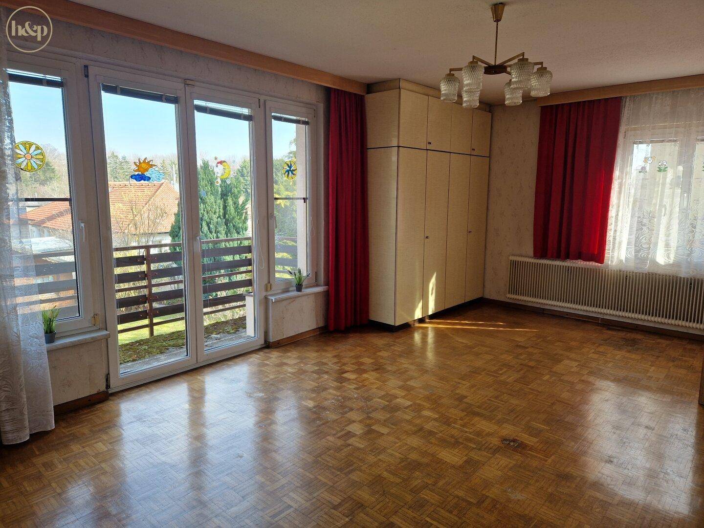 Helles Wohnzimmer mit Parkettboden, großen Fenstern und Zugang zum Balkon.
