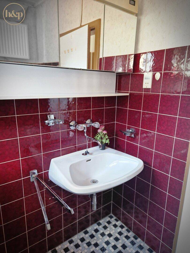 Badezimmer mit roten Fliesen, Einzelwaschbecken und Spiegelschrank.