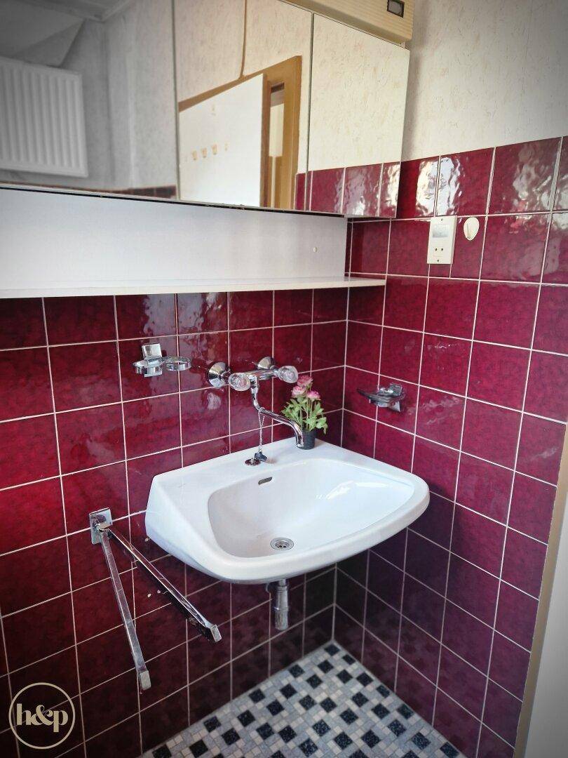 Badezimmer mit roten Fliesen, Waschbecken und Spiegelschrank.
