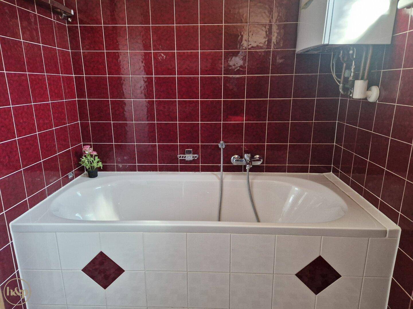 Badezimmer mit roten Wandfliesen und einer eingebauten Badewanne.