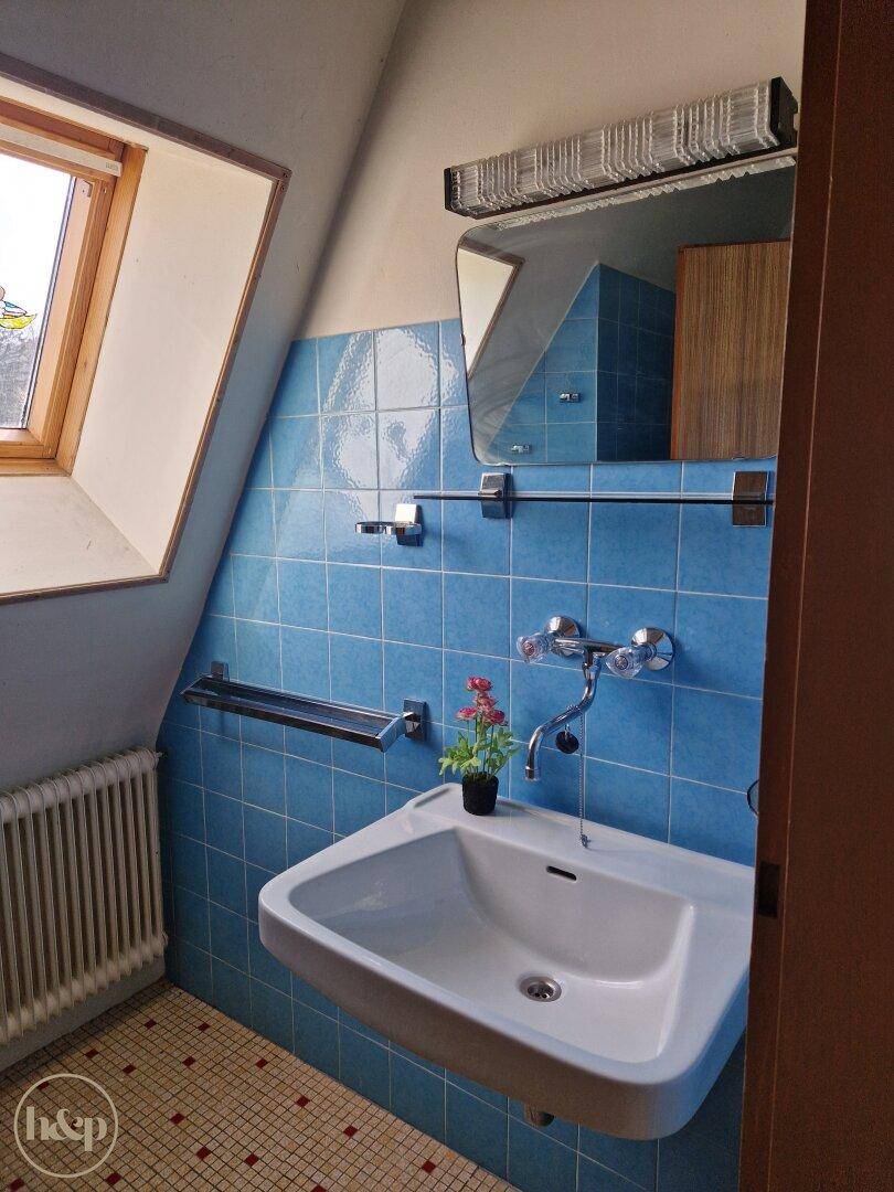 Badezimmer mit blauen Fliesen, Waschbecken, Spiegelschrank und Dachfenster.
