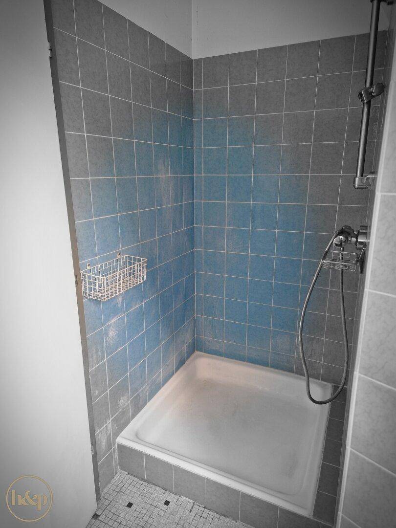 Duschbereich mit blauen und grauen Fliesen und Duschwanne.