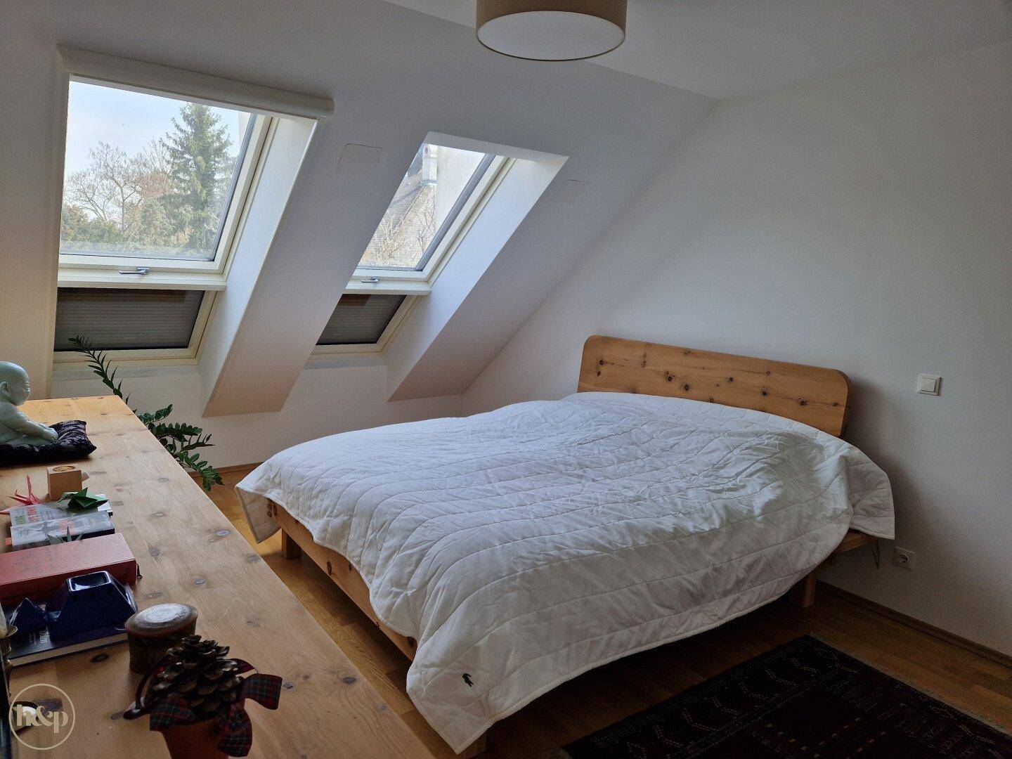 Schlafzimmer mit Holzbett, Holzboden und zwei Dachfenstern unter der Schräge.