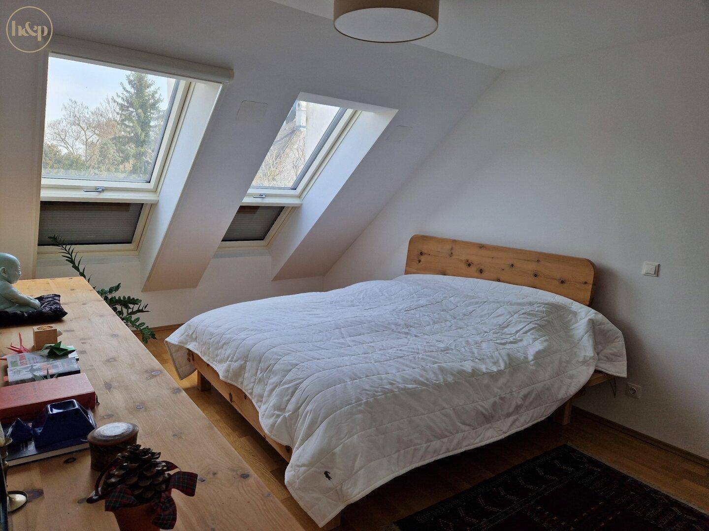 Helles Schlafzimmer im Dachgeschoss mit Holzbett und zwei großen Dachfenstern.