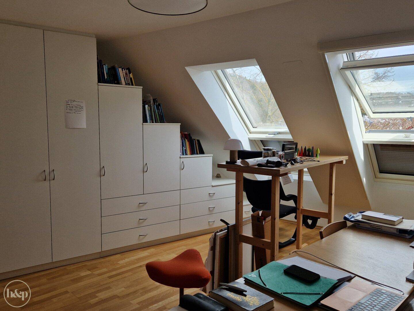 Arbeitszimmer mit Einbauschränken, Schreibtisch und Dachfenstern unter der Schräge.