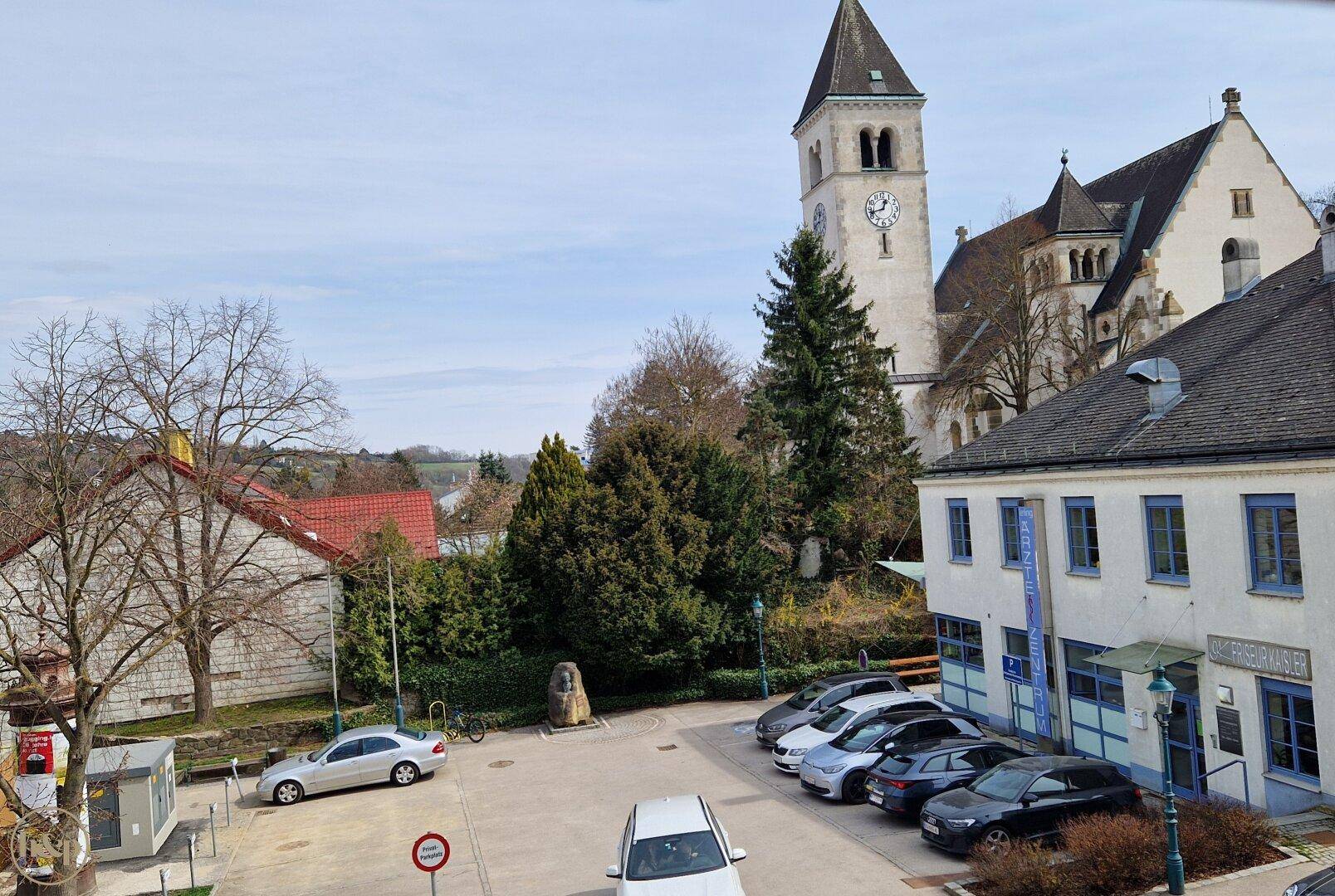 Panoramablick auf einen Stadtplatz mit historischer Kirche und parkenden Autos.
