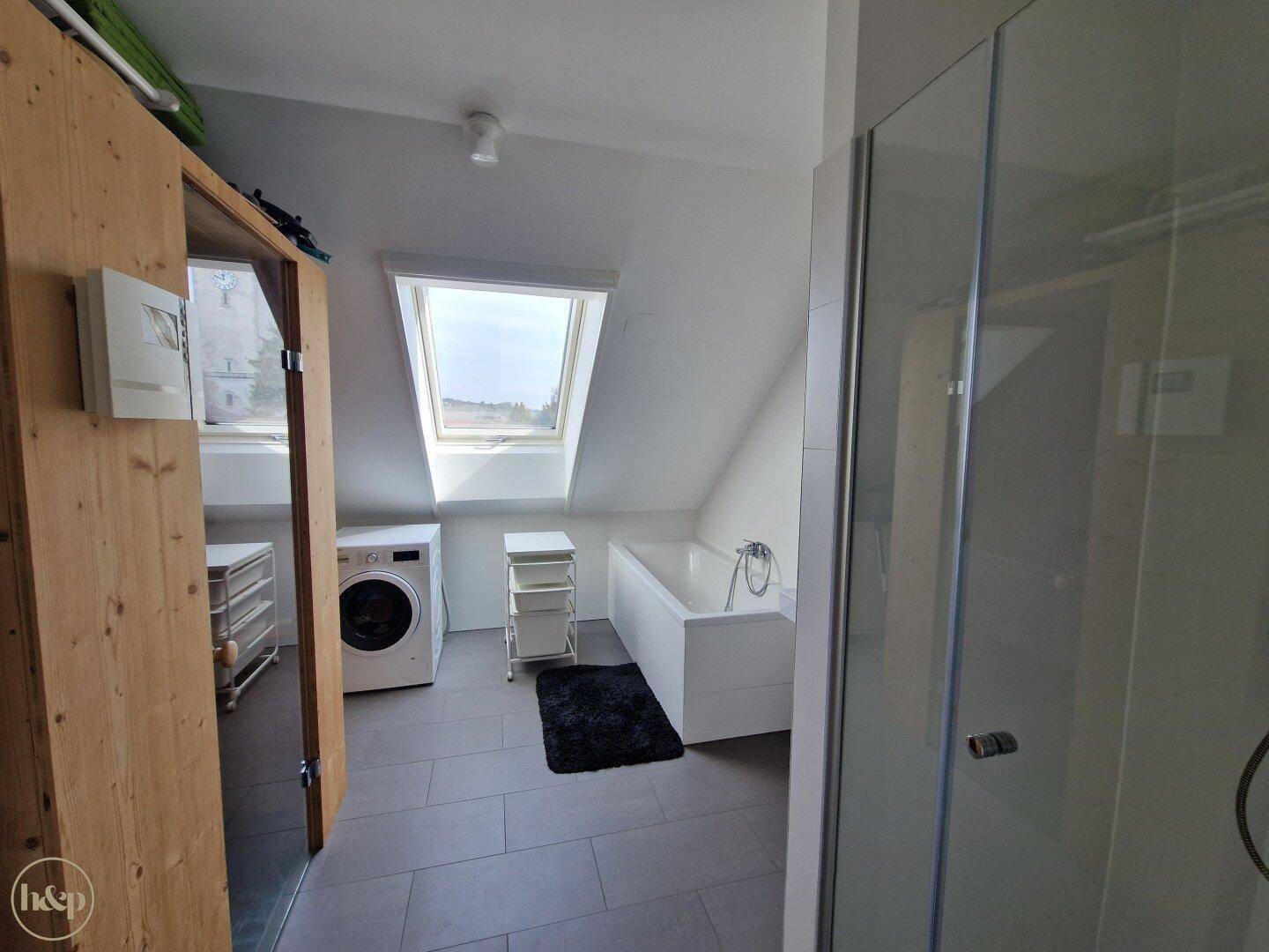 Helles Badezimmer mit Badewanne, Dusche und Waschmaschine unter Dachschrägen.