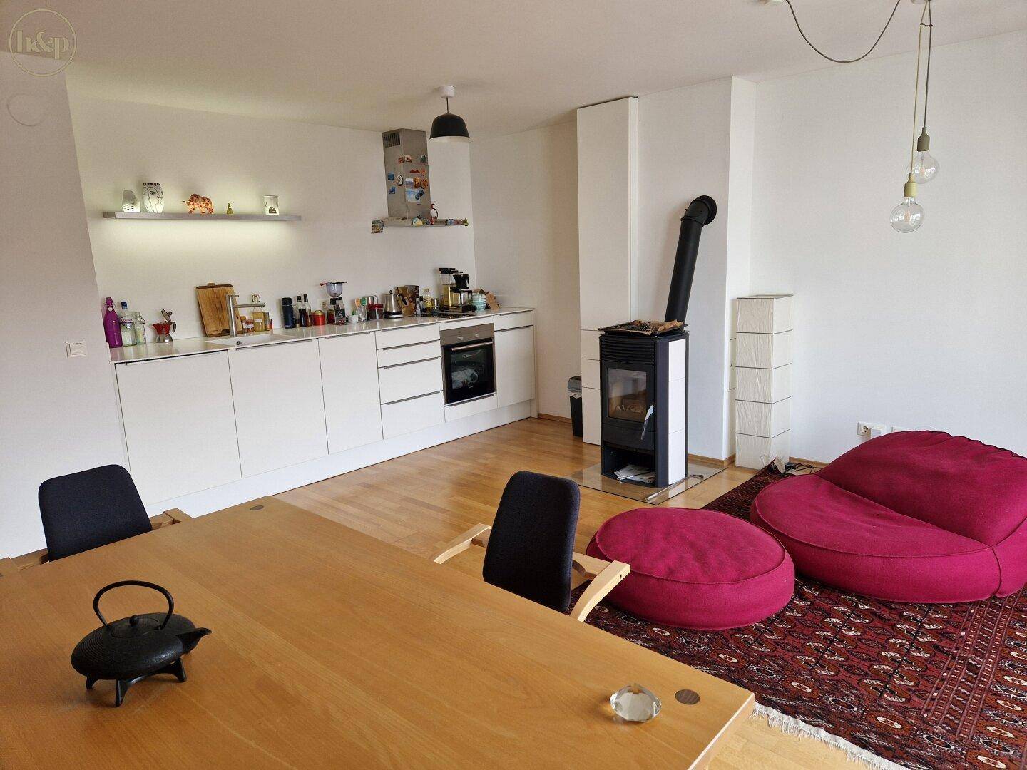 Offener Wohn-Essbereich mit moderner Einbauküche, Kaminofen und gemütlicher Sitzecke.