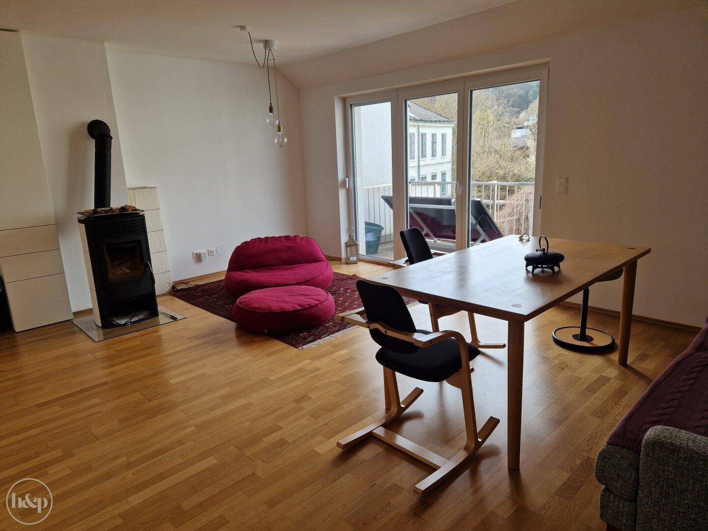 Geräumiger Wohn-Essbereich mit Holzboden, Kaminofen und Balkonzugang.