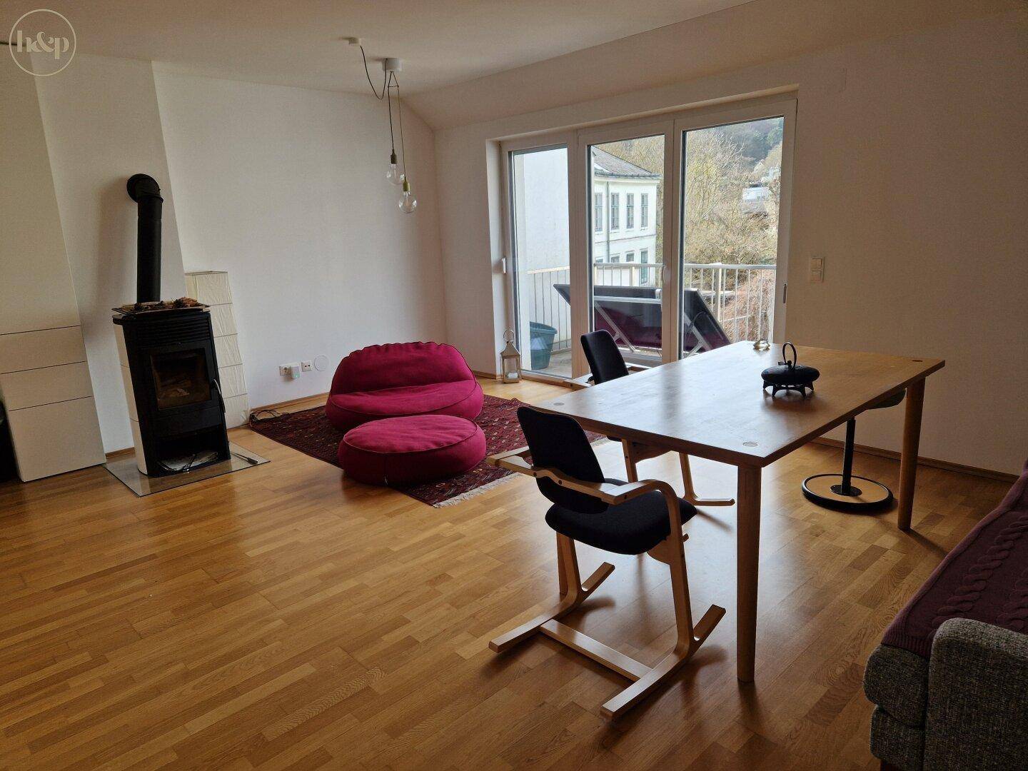 Geräumiger Wohn-Essbereich mit Kaminofen, Holzboden und Zugang zum Balkon.