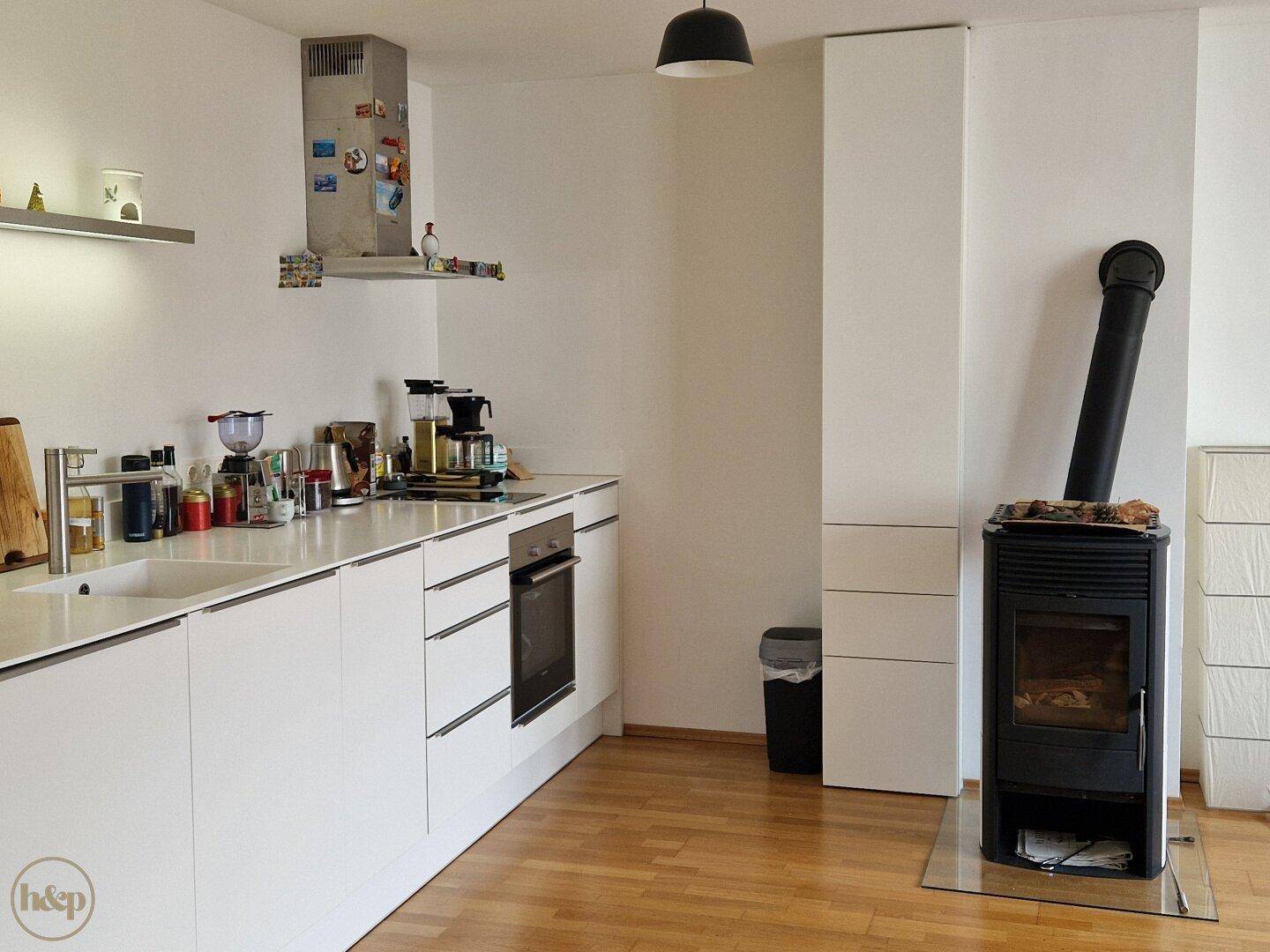 Moderne weiße Küche mit Holzboden und integriertem Kaminofen.