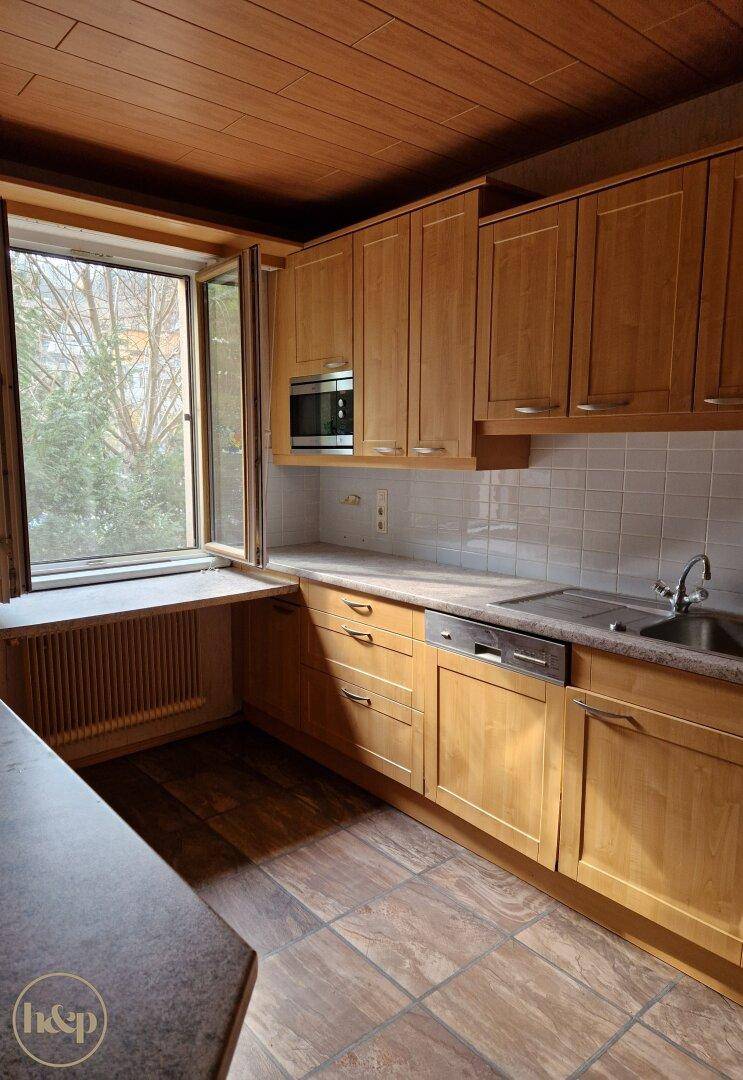 Helle Küche mit Holzschränken, Einbaugeräten und Fenster mit Blick ins Grüne.