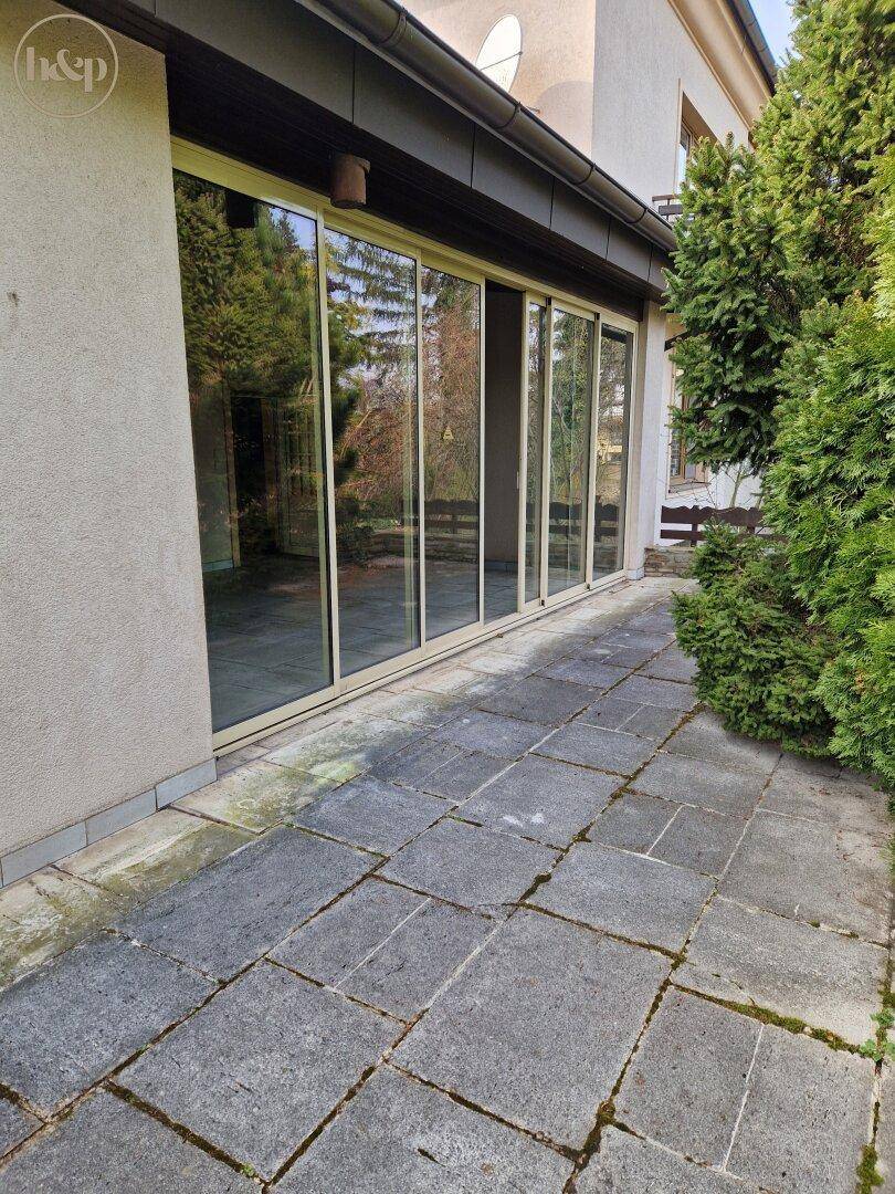 Hausfassade mit großen Glasschiebetüren, die zur gepflasterten Terrasse führen.