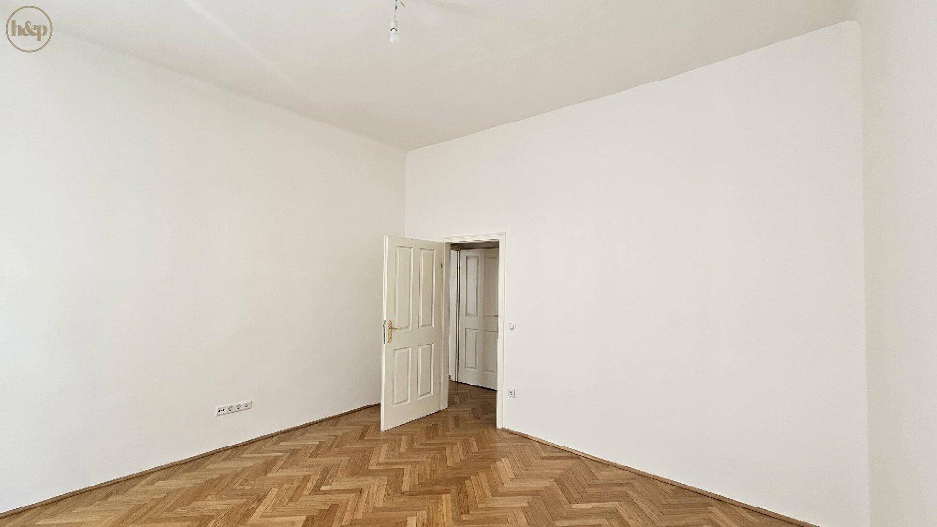 Leeres Zimmer mit Fischgrätparkett und einer geöffneten Tür, bereit zur Einrichtung.