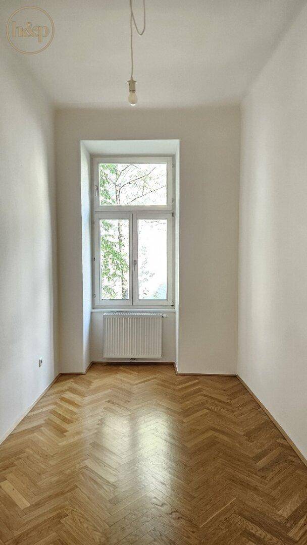 Freundliches Zimmer mit klassischem Fischgrätparkett und einem großen Fenster, ideal als Schlafzimmer.
