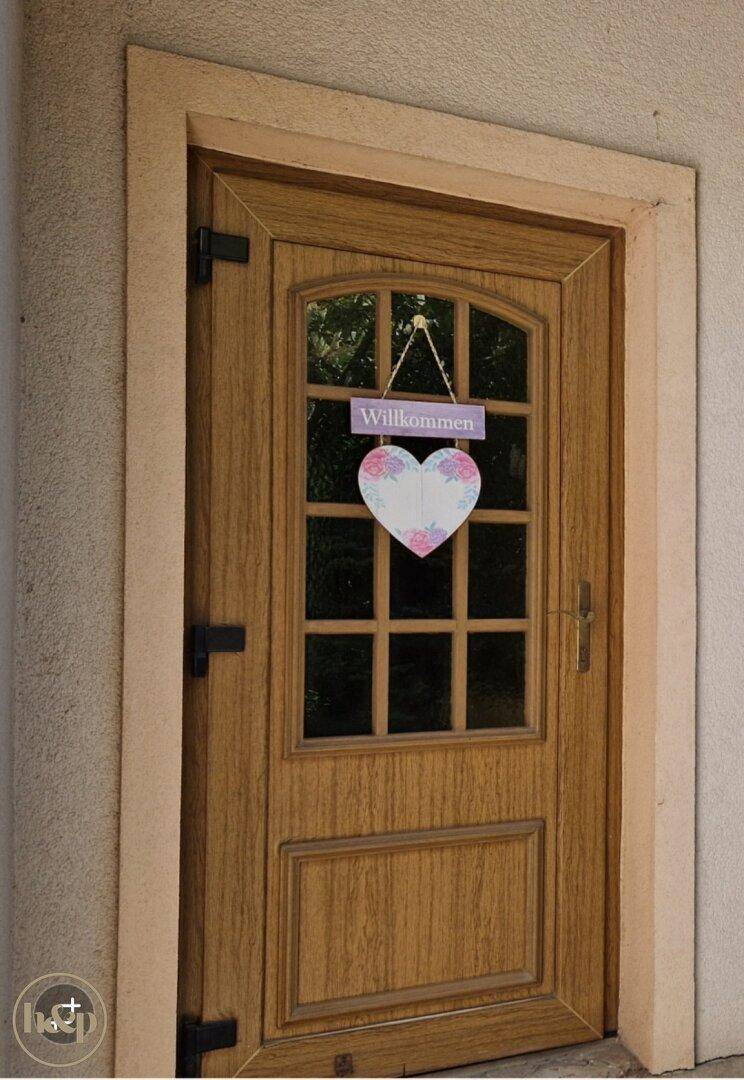 Nahaufnahme der Holztür mit Glasausschnitten und einem herzlichen 'Willkommen'-Schild.