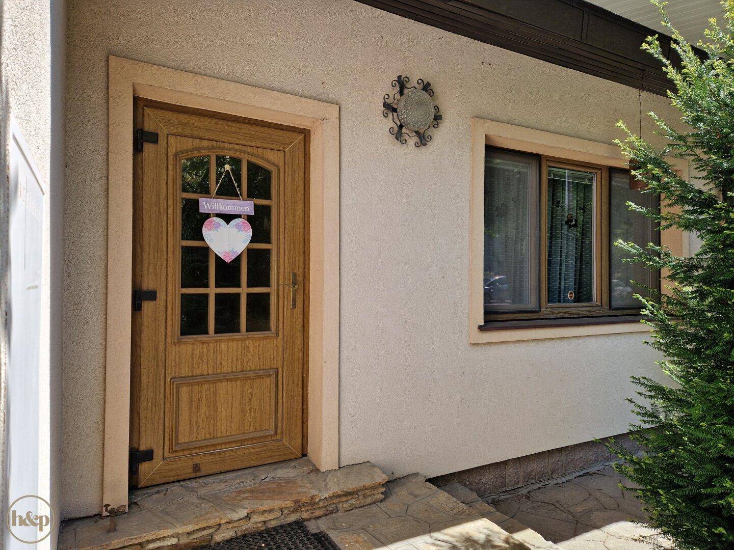 Eingangsbereich des Hauses mit Holztür und einem Willkommensschild in Herzform.