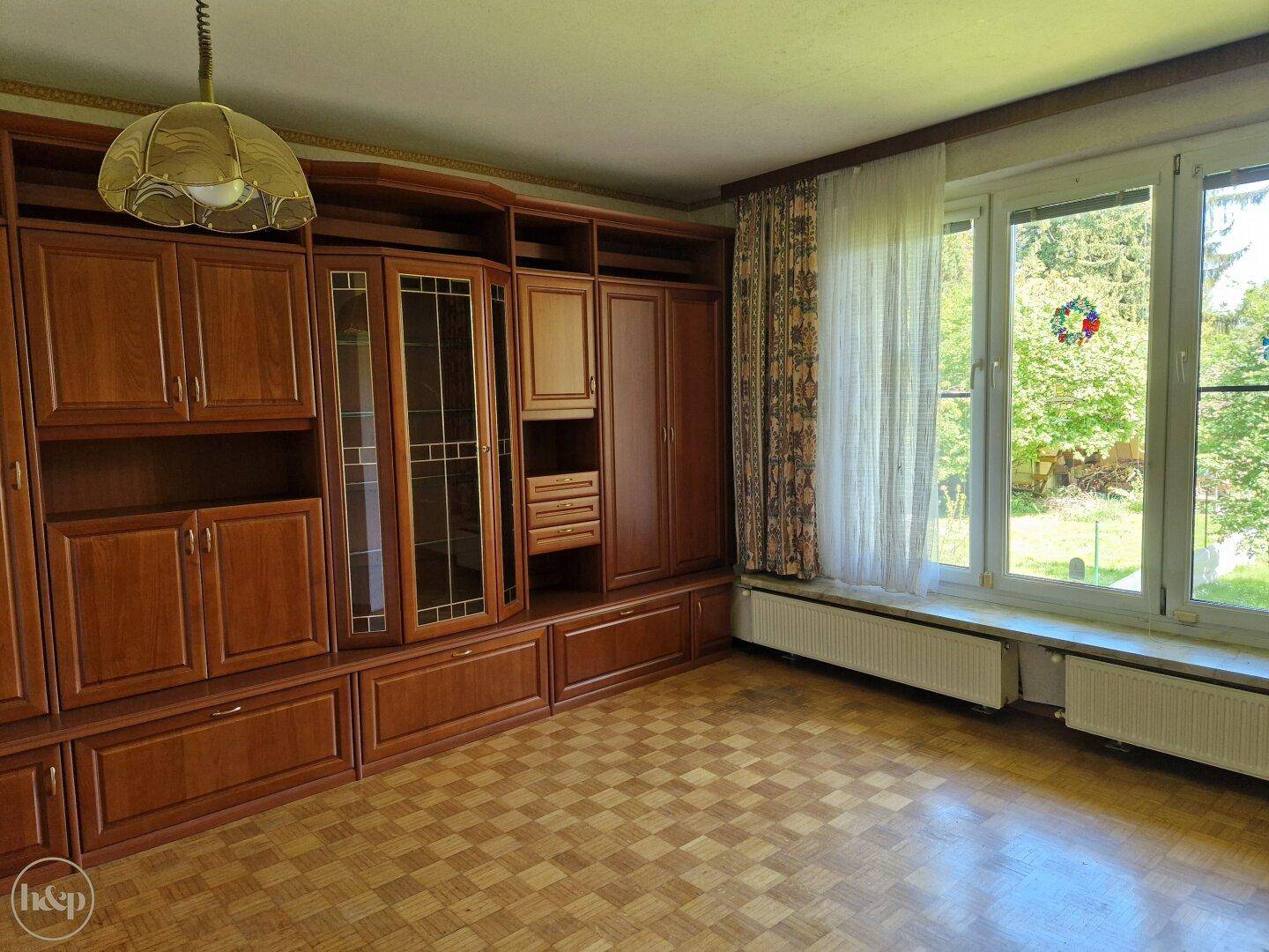 Wohnzimmer mit großer Holzschrankwand, Parkettboden und Blick ins Grüne.