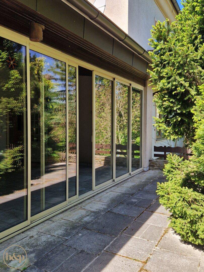 Helle Terrasse mit großen Glasschiebetüren, die die umliegende Natur und Bäume widerspiegeln.