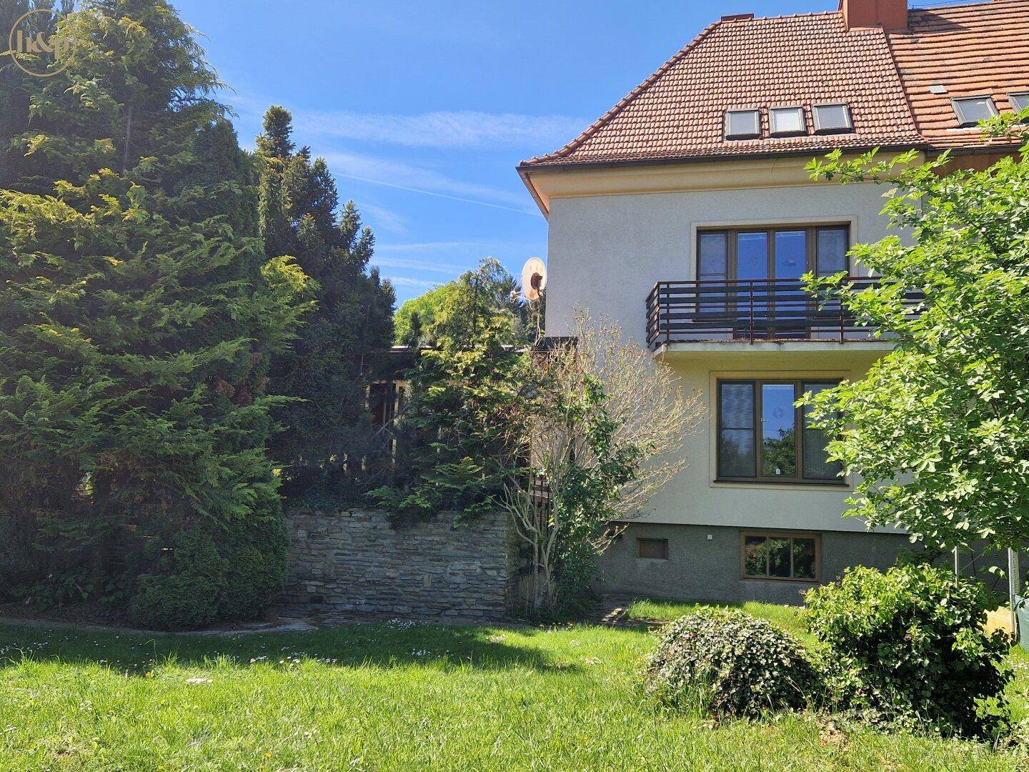 Grüner Gartenbereich mit Rasen und Bäumen, im Hintergrund das Haus mit Balkon.