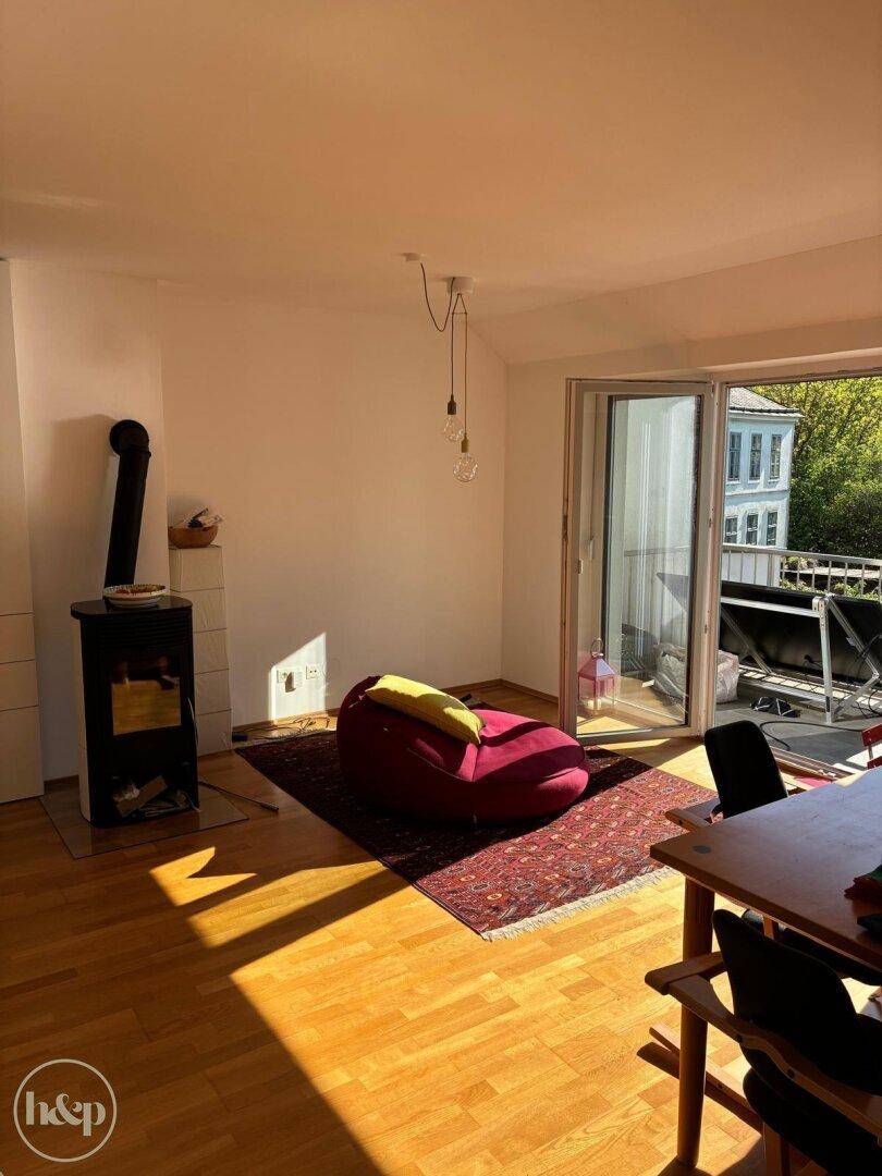 Sonniges Wohnzimmer mit Holzboden, Kaminofen und Zugang zum Balkon.