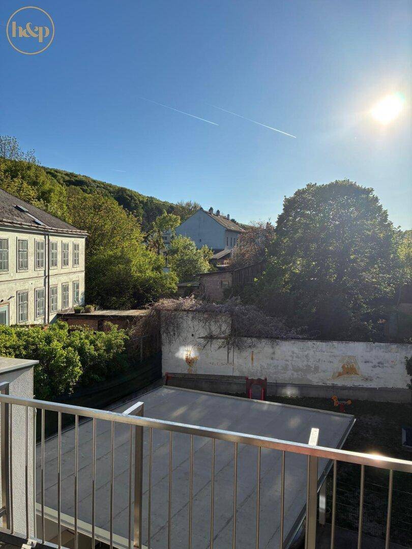 Sonniger Ausblick vom Balkon auf grüne Hügel und umliegende Gebäude.