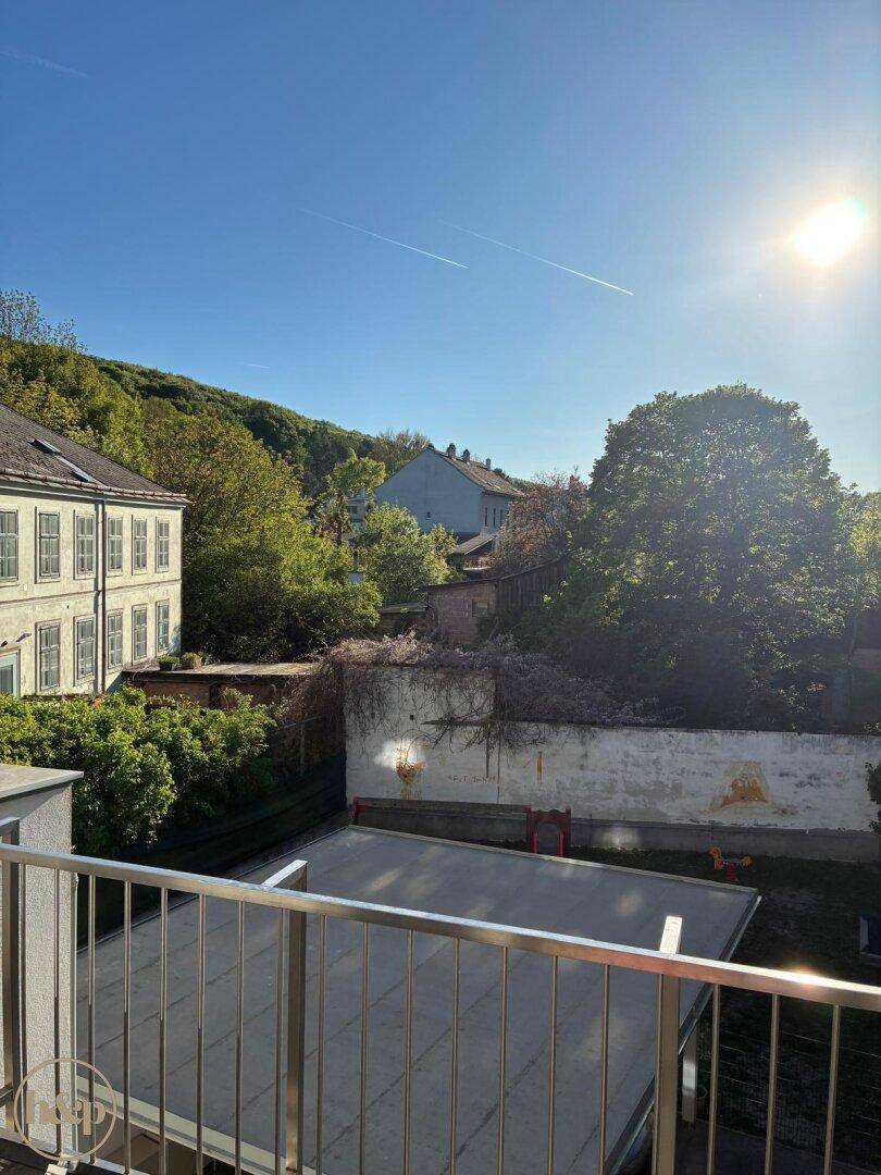 Sonniger Ausblick vom Balkon auf grüne Hügel und umliegende Gebäude.