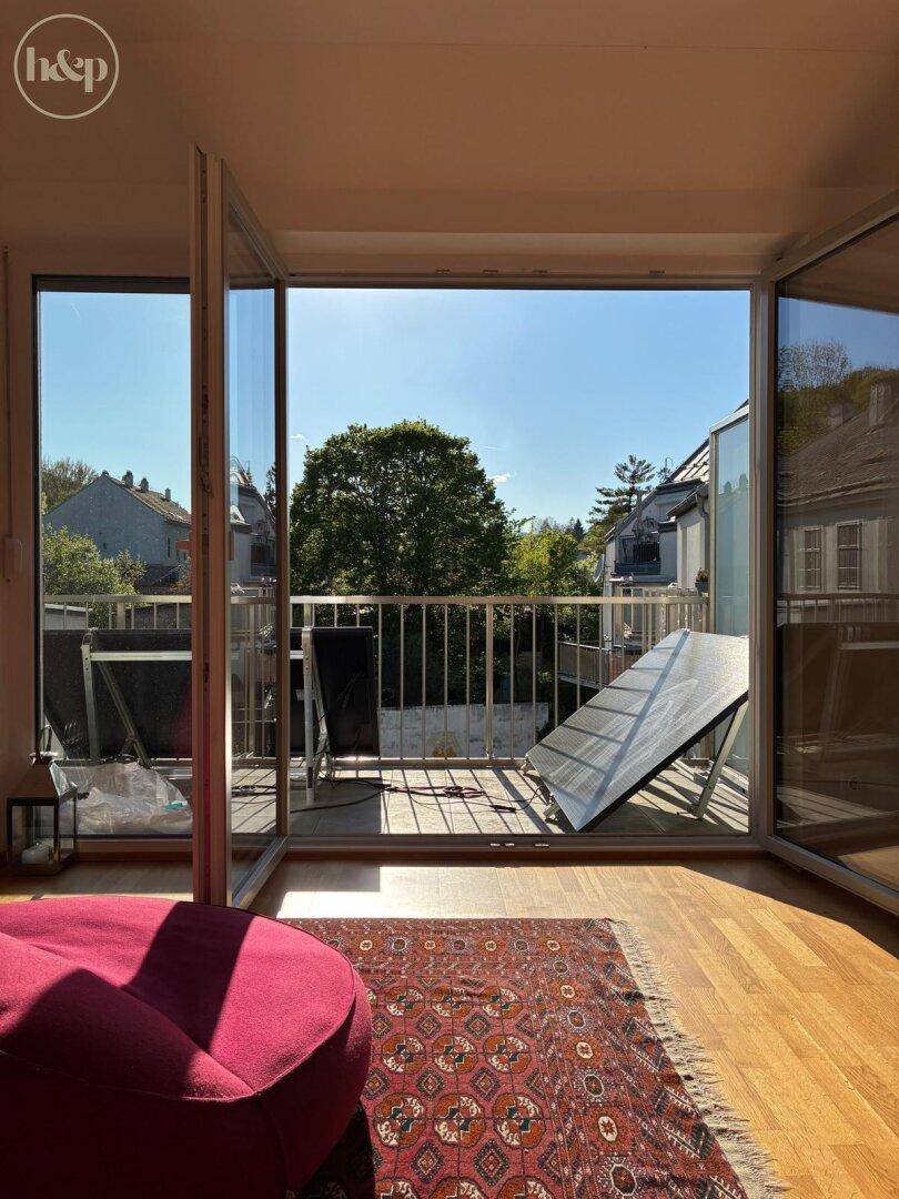 Heller Wohnbereich mit großem Fenster zum Balkon, auf dem ein Solarmodul steht.