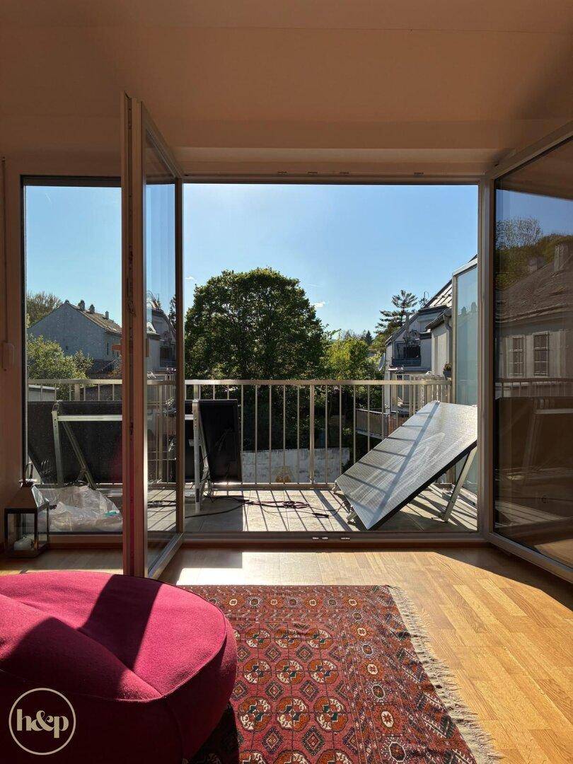 Helles Wohnzimmer mit Holzboden und Blick auf den sonnigen Balkon mit Solarmodulen.