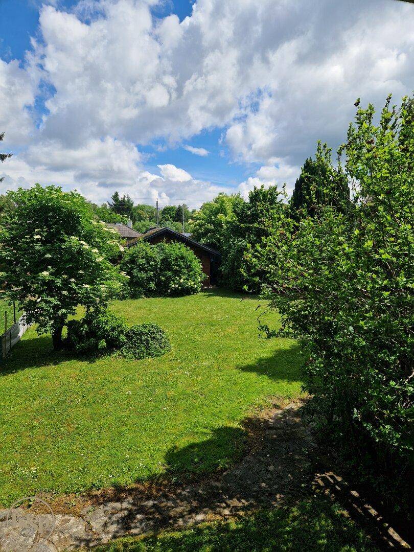 Großer, gepflegter Garten mit Rasenfläche und Bäumen unter bewölktem Himmel.