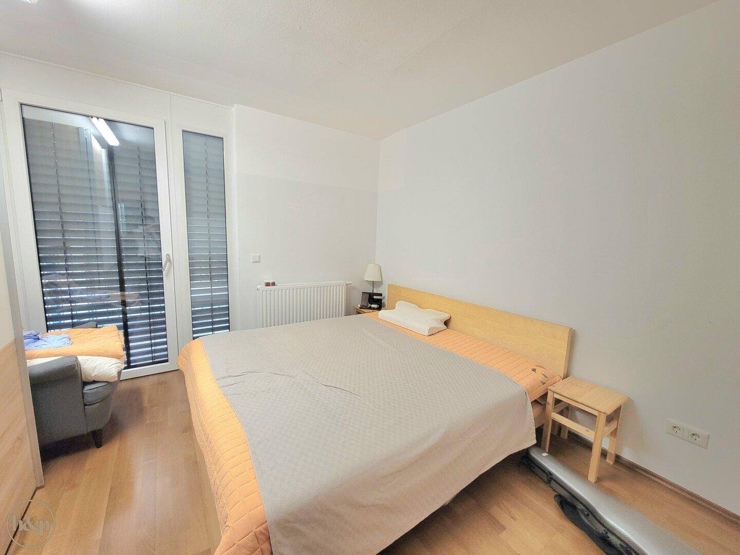 Helles Schlafzimmer mit Holzboden, großem Fenster und Zugang zu einem Balkon oder einer Terrasse.