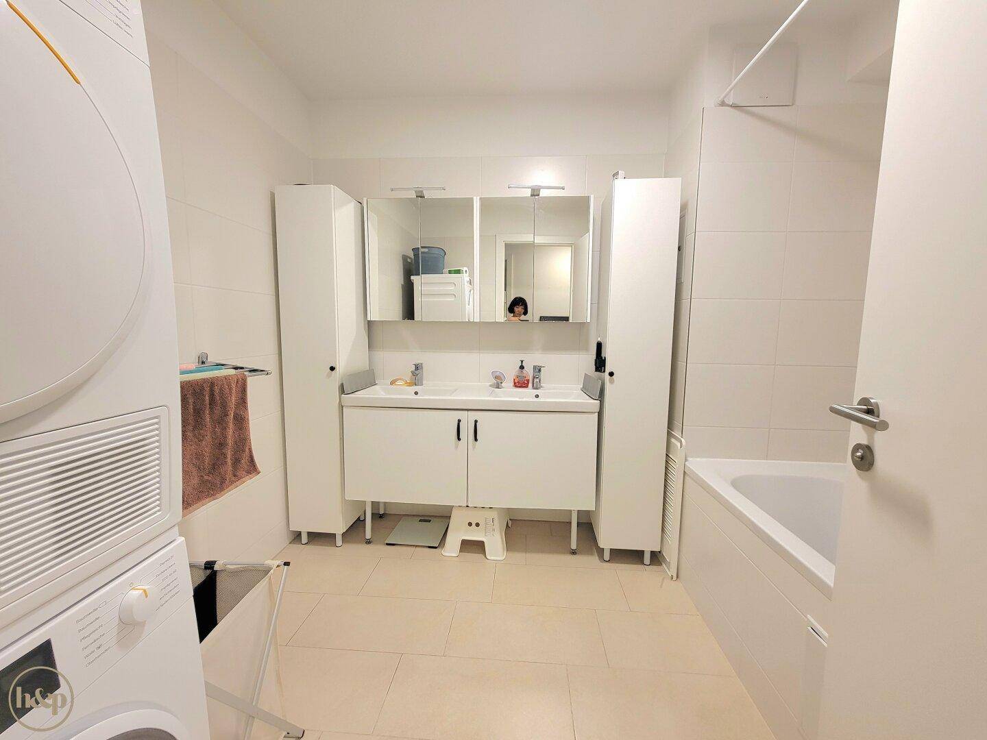 Modernes Badezimmer mit Doppelwaschbecken, Badewanne und integrierter Waschmaschine und Trockner.