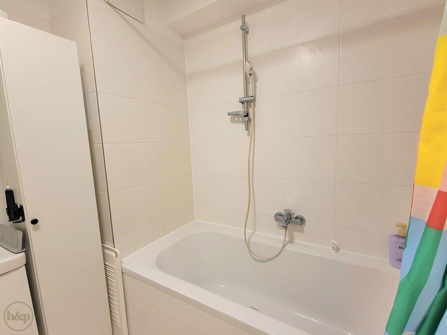 Saubere Badewanne mit Duschfunktion in einem hell gefliesten Badezimmer, praktisch und funktional.