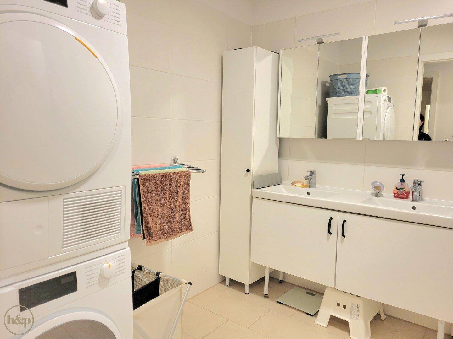 Funktionales Badezimmer mit Doppelwaschbecken, Waschmaschine und Trockner, hell gefliest und gut ausgestattet.