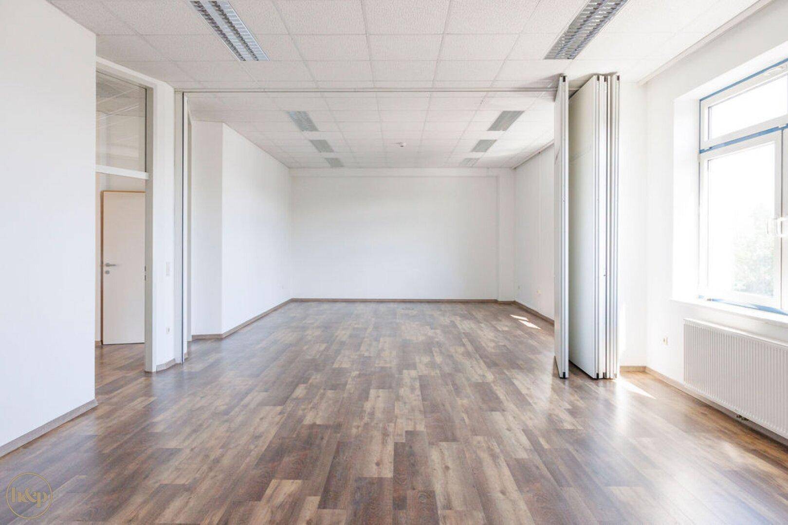 Flexibler Büroraum mit verschiebbarer Trennwand, hellen Wänden und Laminatboden.
