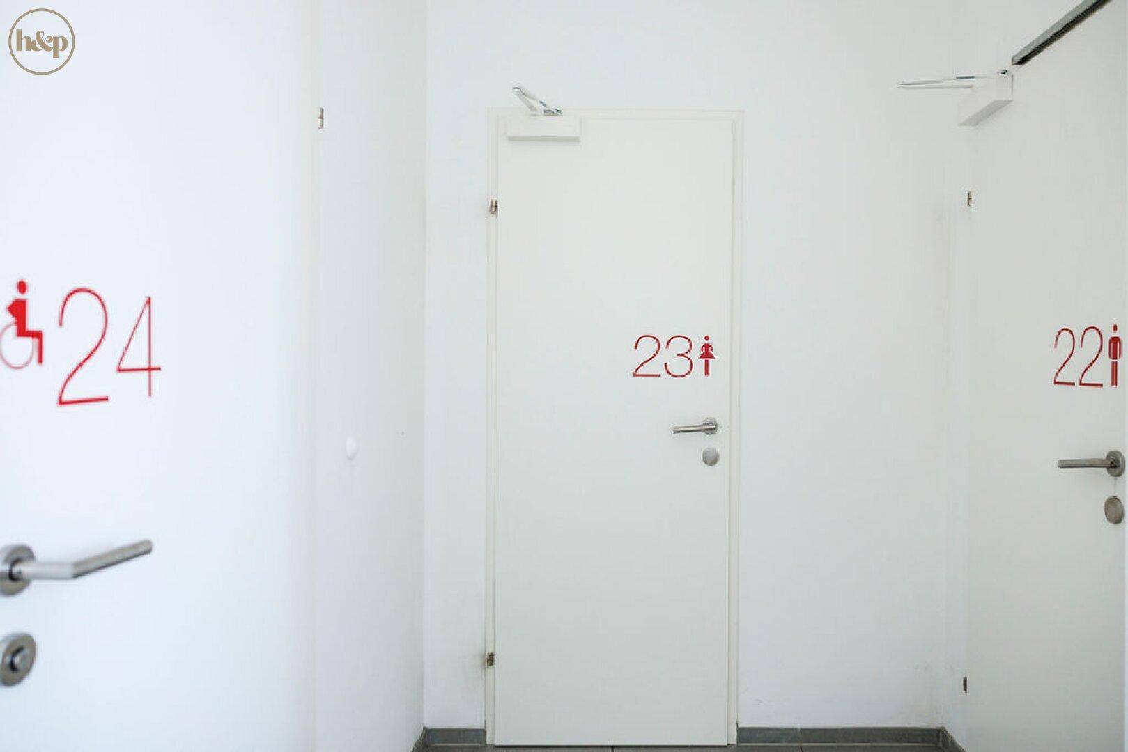 Flur mit mehreren Türen, nummeriert und mit Piktogrammen für Toiletten.