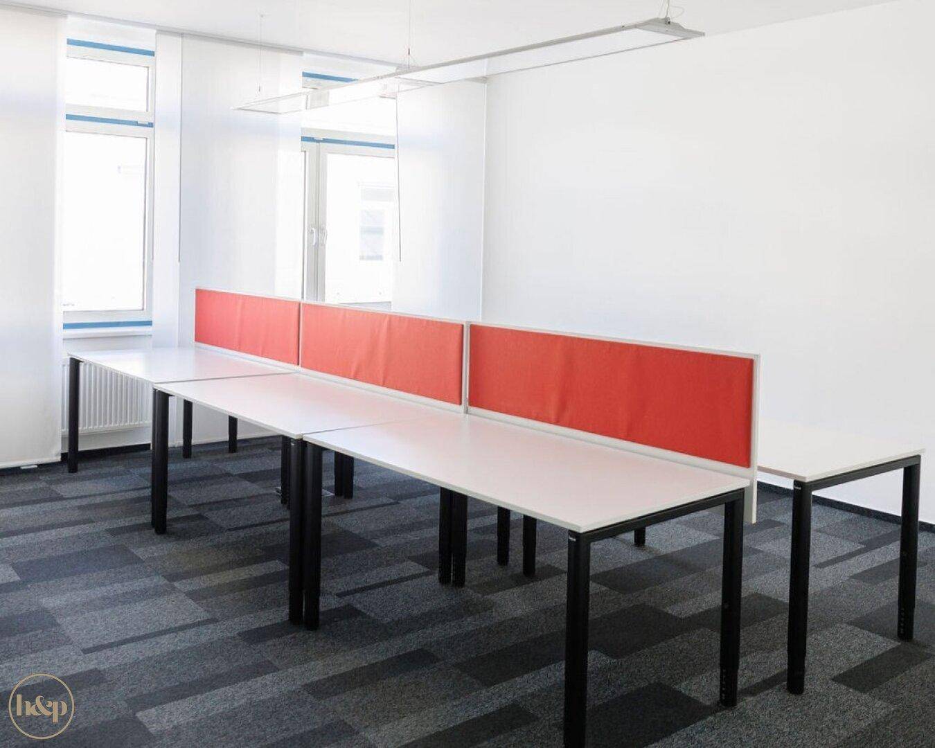 Geräumiger, leerer Bürobereich mit langen Schreibtischen und roten Trennwänden, bereit für neue Mieter.