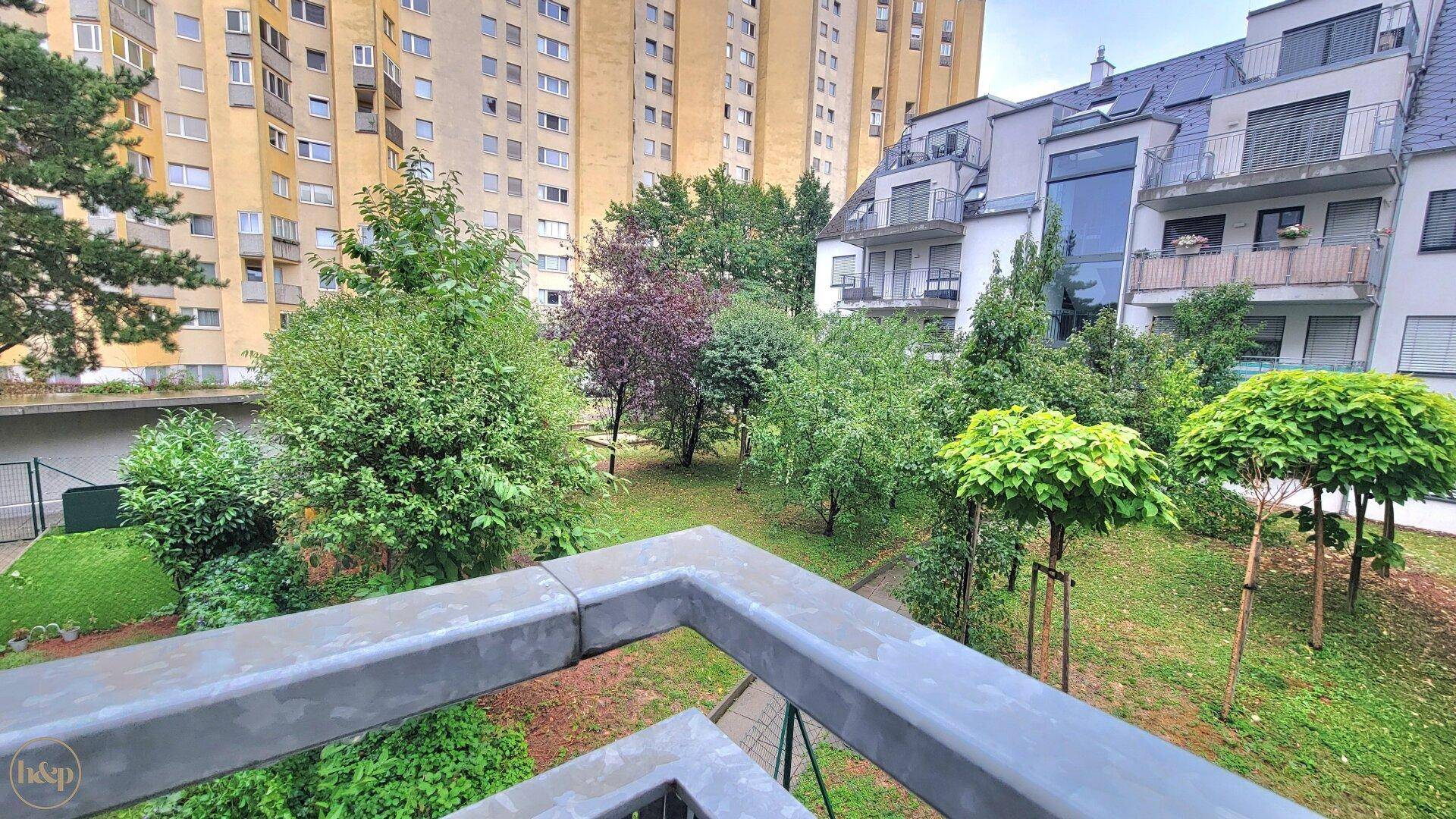 Blick vom Balkon auf einen grünen Innenhof mit Bäumen und umliegenden Wohngebäuden.