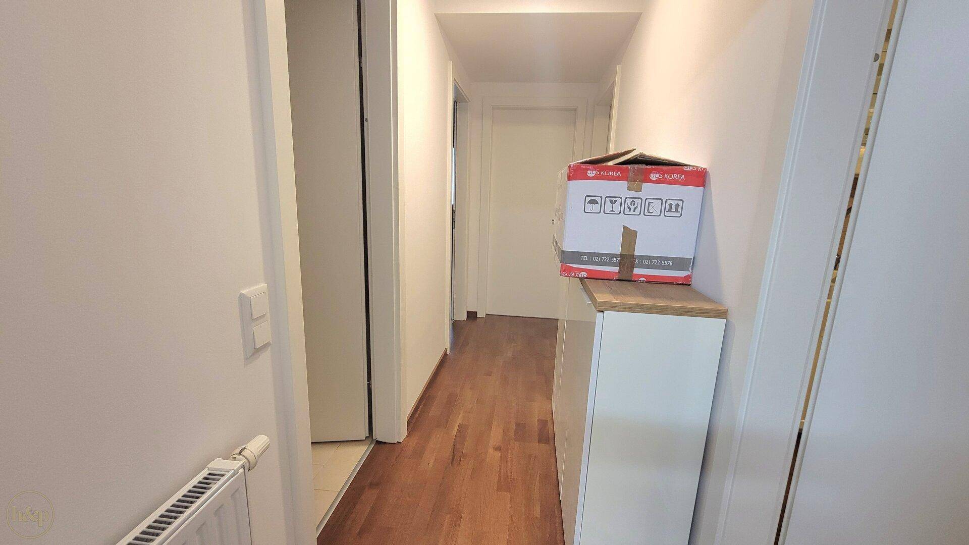Langer Flur mit Holzboden und einem kleinen Schrank, der zusätzlichen Stauraum bietet.