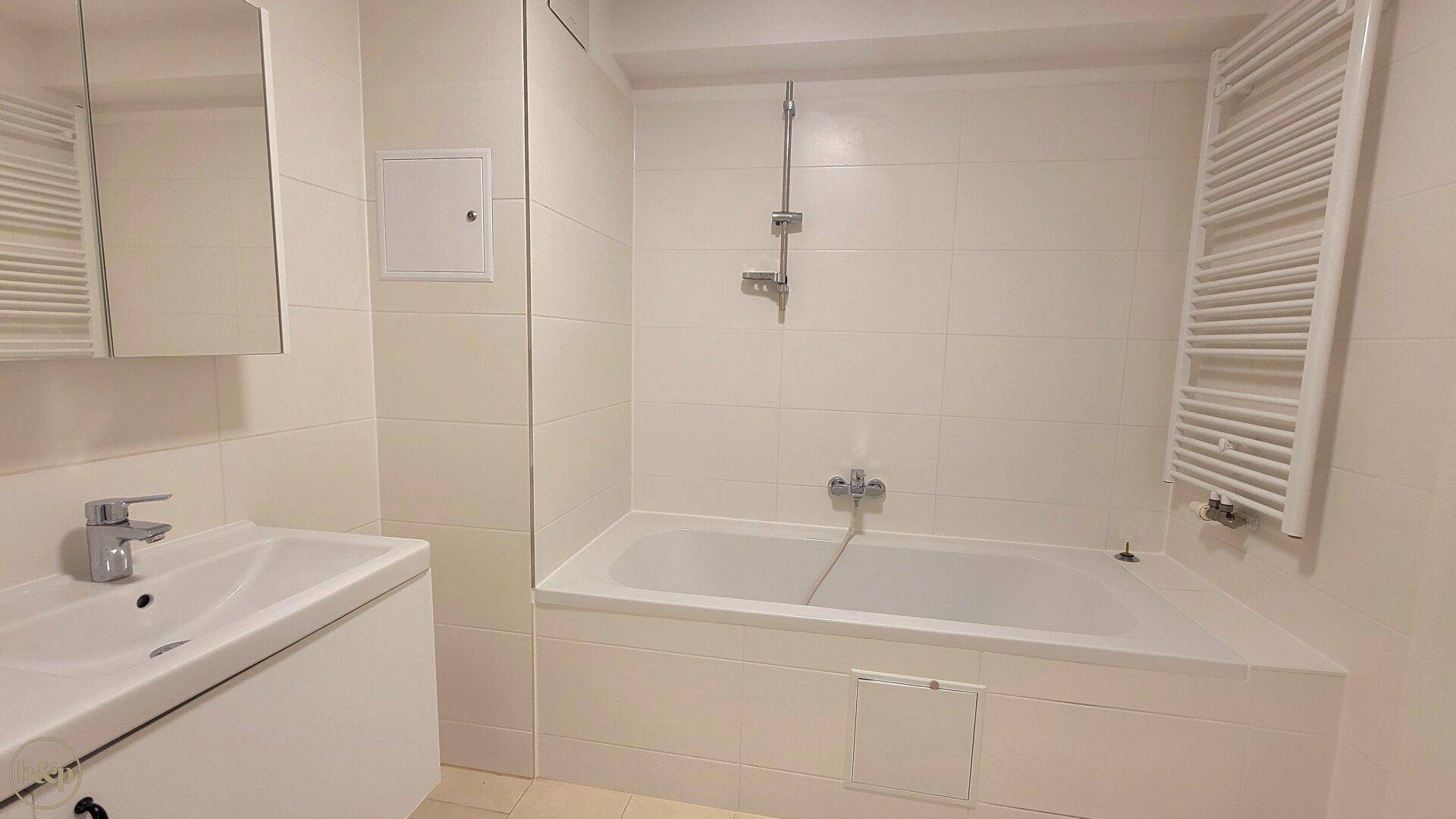 Helles Badezimmer mit Badewanne, Einzelwaschbecken und beheiztem Handtuchhalter.