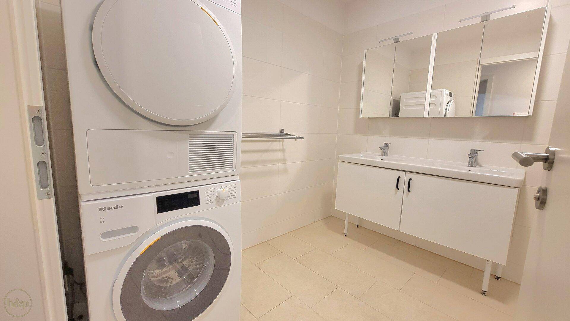 Modernes Badezimmer mit Waschmaschine, Trockner, Doppelwaschbecken und Spiegelschränken.