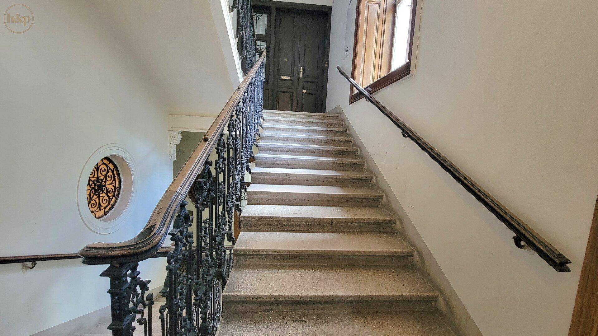 Elegantes Treppenhaus mit schmiedeeisernem Geländer und Steinstufen in einem Altbau.