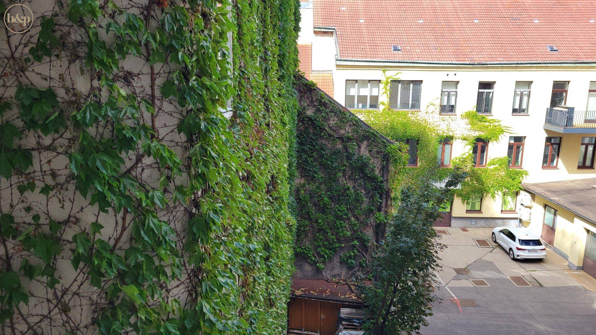 Innenhof mit begrünten Wänden und parkenden Autos, umgeben von Gebäuden.