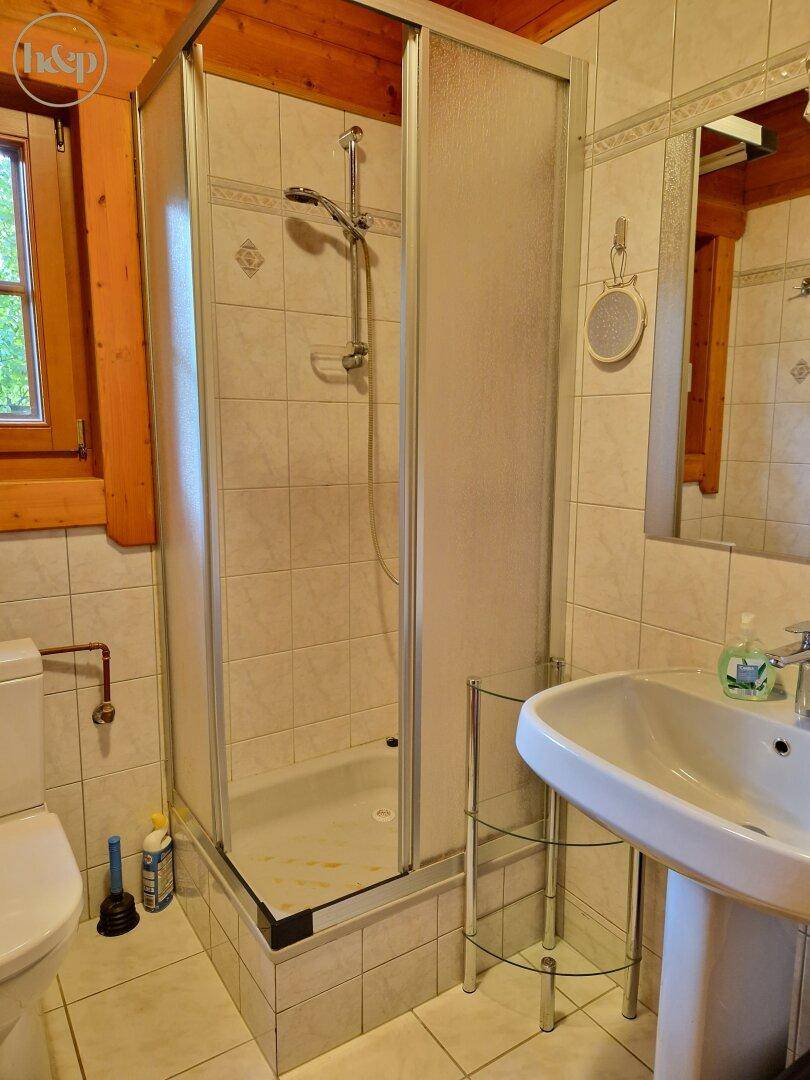 Badezimmer mit Duschkabine, WC und Waschbecken, hell gefliest.