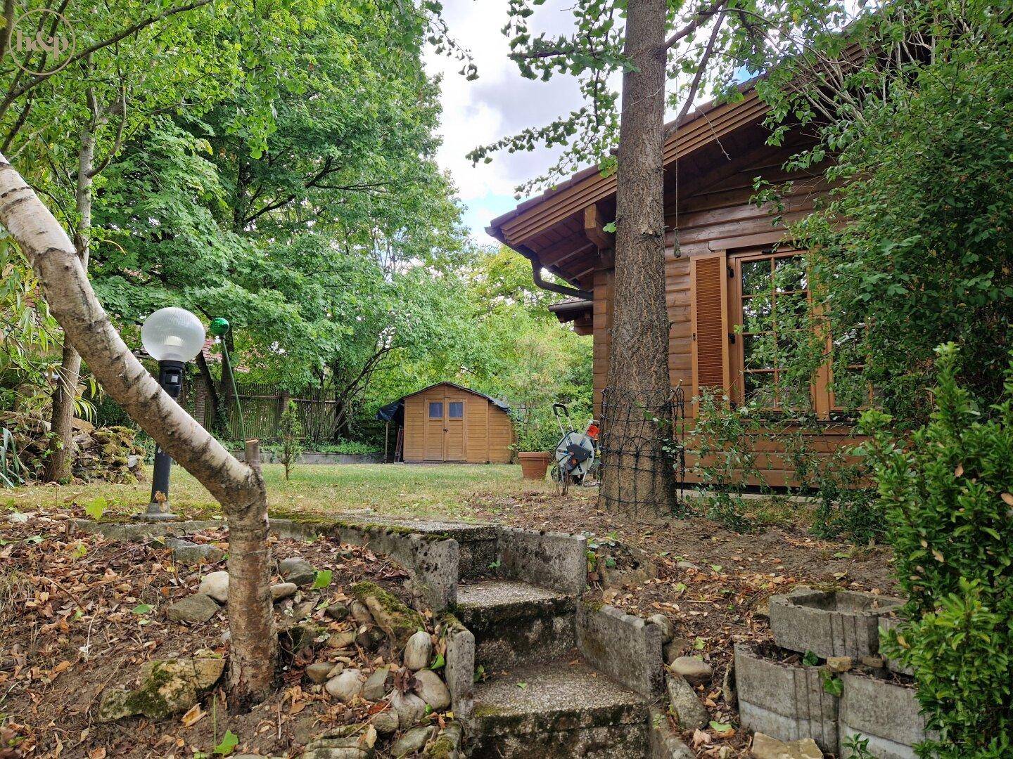 Gartenansicht mit Steintreppe, die zum Haus und Schuppen führt, umgeben von Grün.
