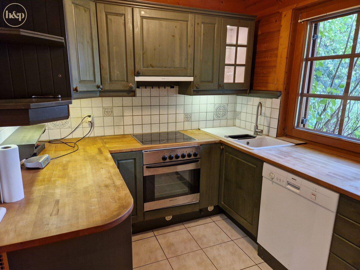 Traditionelle Küche mit grünen Holzschränken, Holzarbeitsplatten und Fenster.