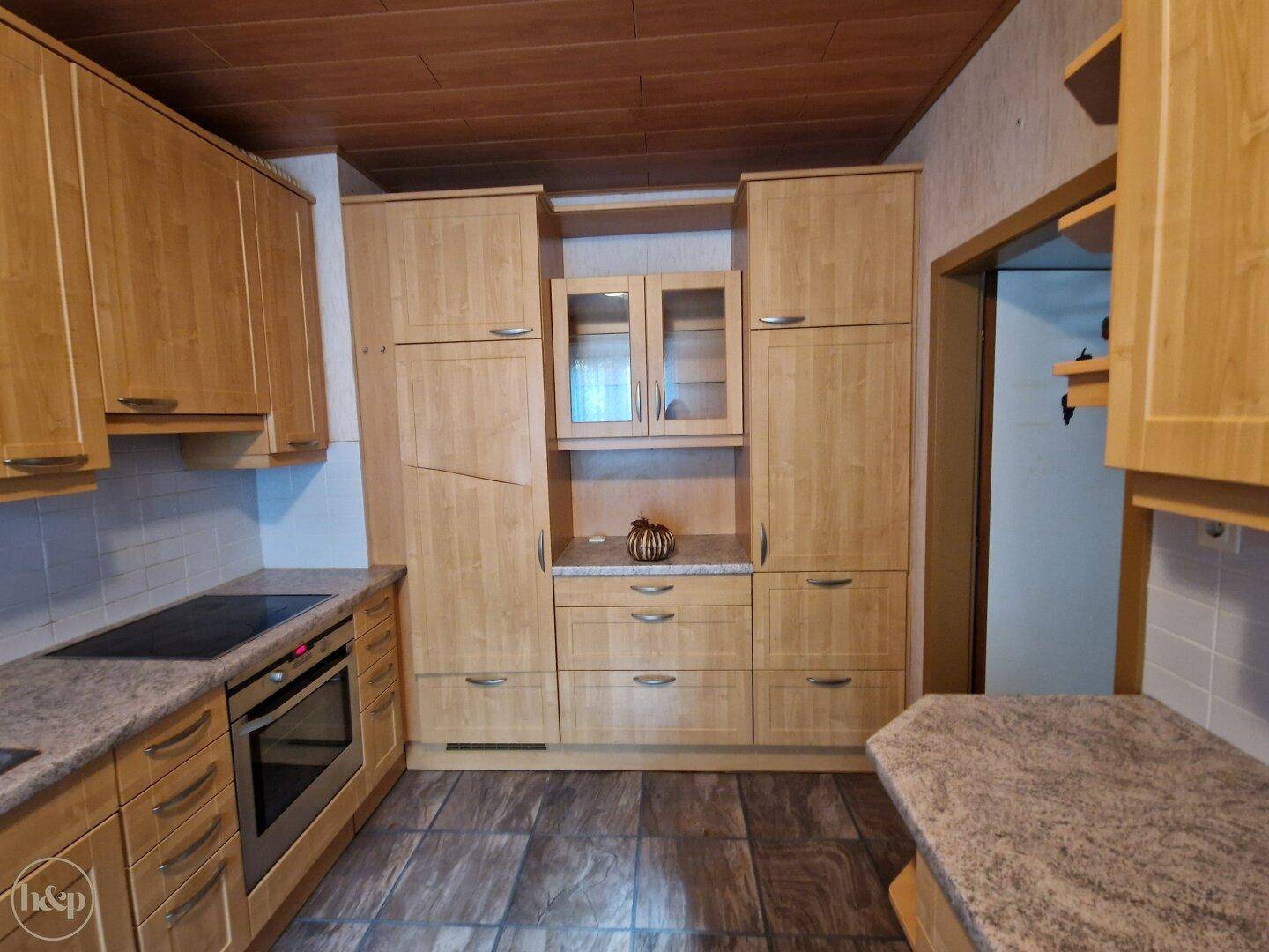 Geräumige Küche mit vielen Holzschränken, integrierten Geräten und dunklem Fliesenboden.